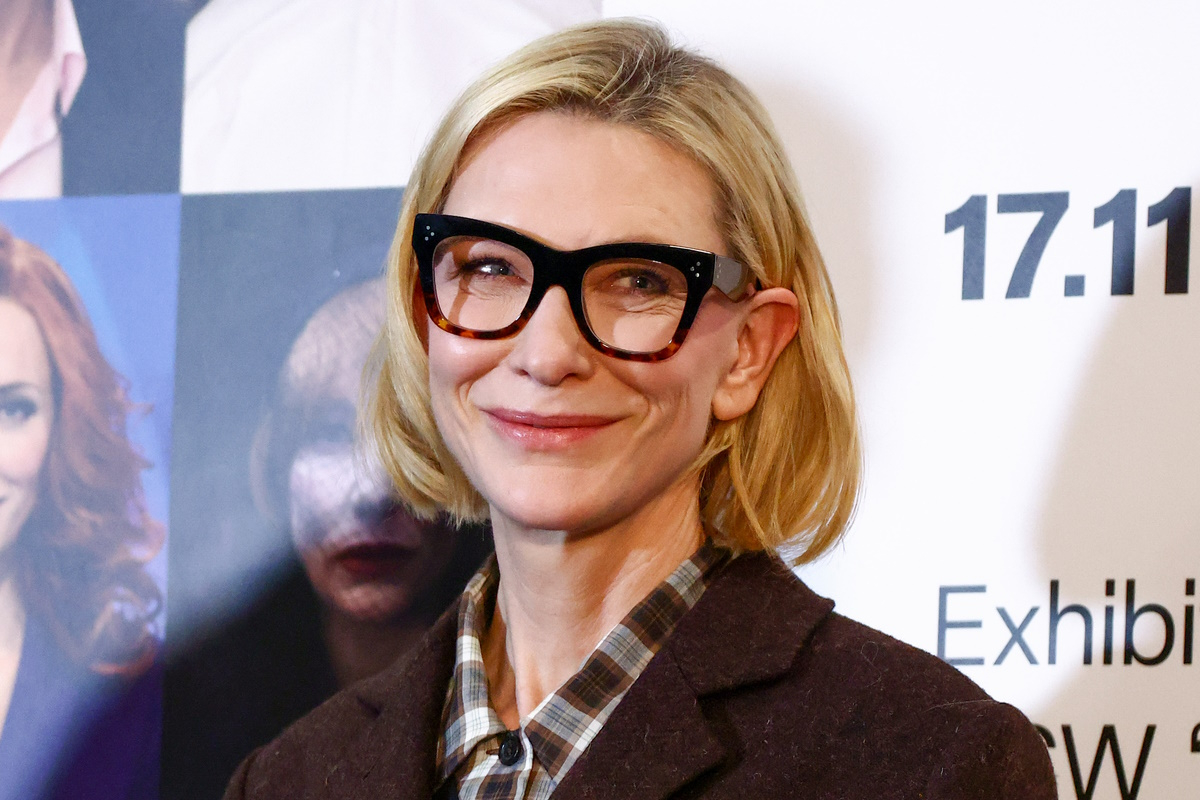 Cate Blanchett prezentuje w Łodzi elegancki garnitur damski w modnym odcieniu brązu na zimę 2025 roku. Ma na  sobie również koszule w kratę i modne okulary korekcyjne.