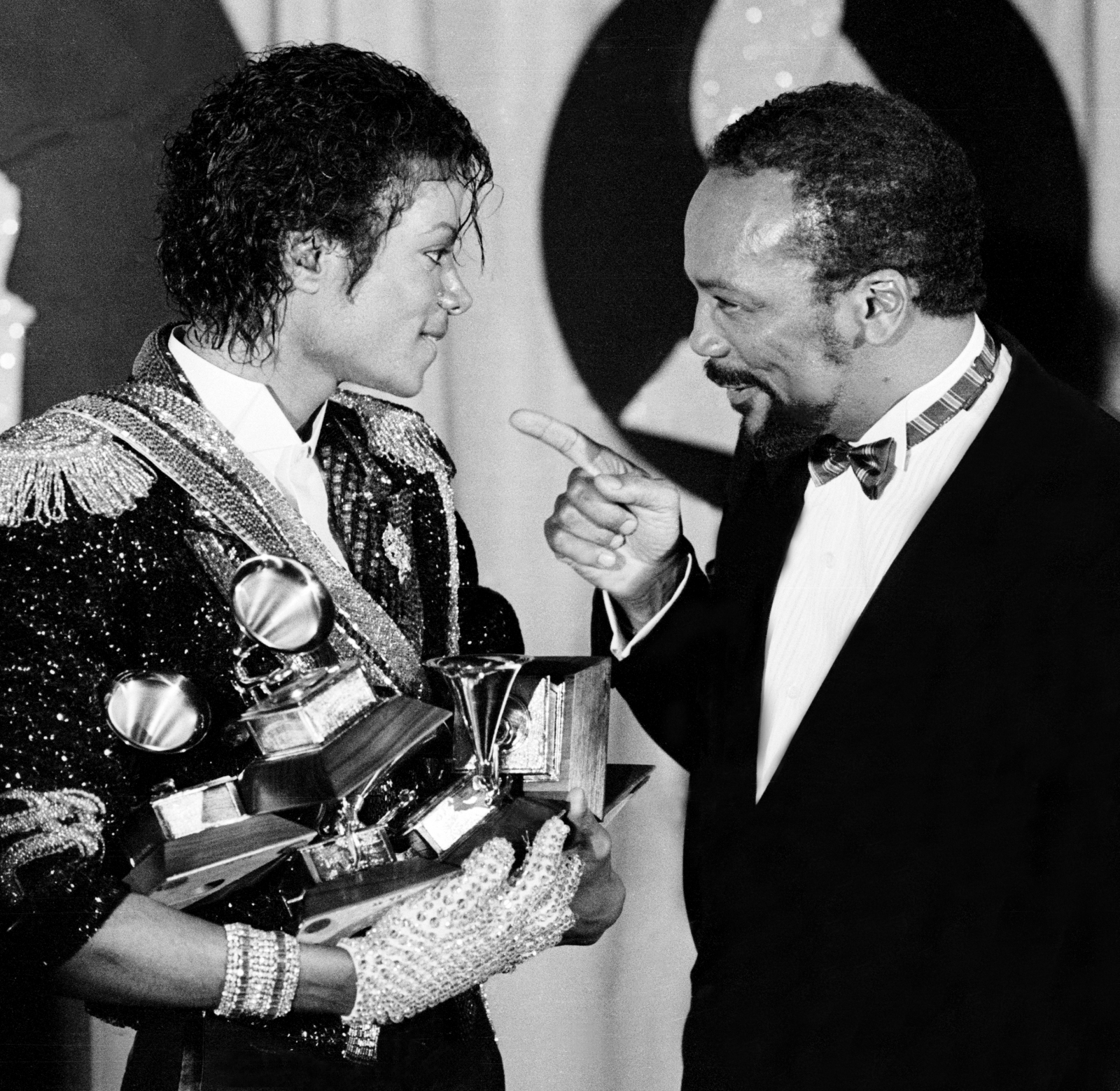 Michael Jackson i Quincy Jones rozmawiają, trzymając statuetki Grammy, w atmosferze radości i sukcesu.