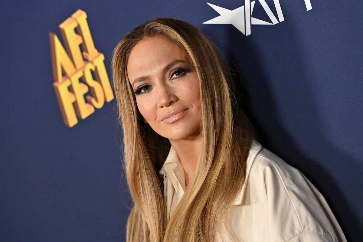 Jennifer Lopez z długimi włosami w jasnej bluzie, pozująca na tle logo AFI FEST.