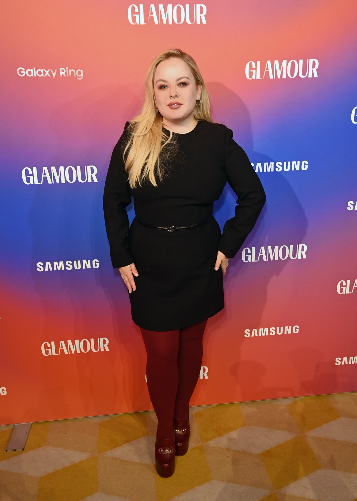 Aktorka Nicola Coughlan w modnych burgundowych rajstopach na jesień i zimę 2024 na tle banerów Glamour i Samsung.