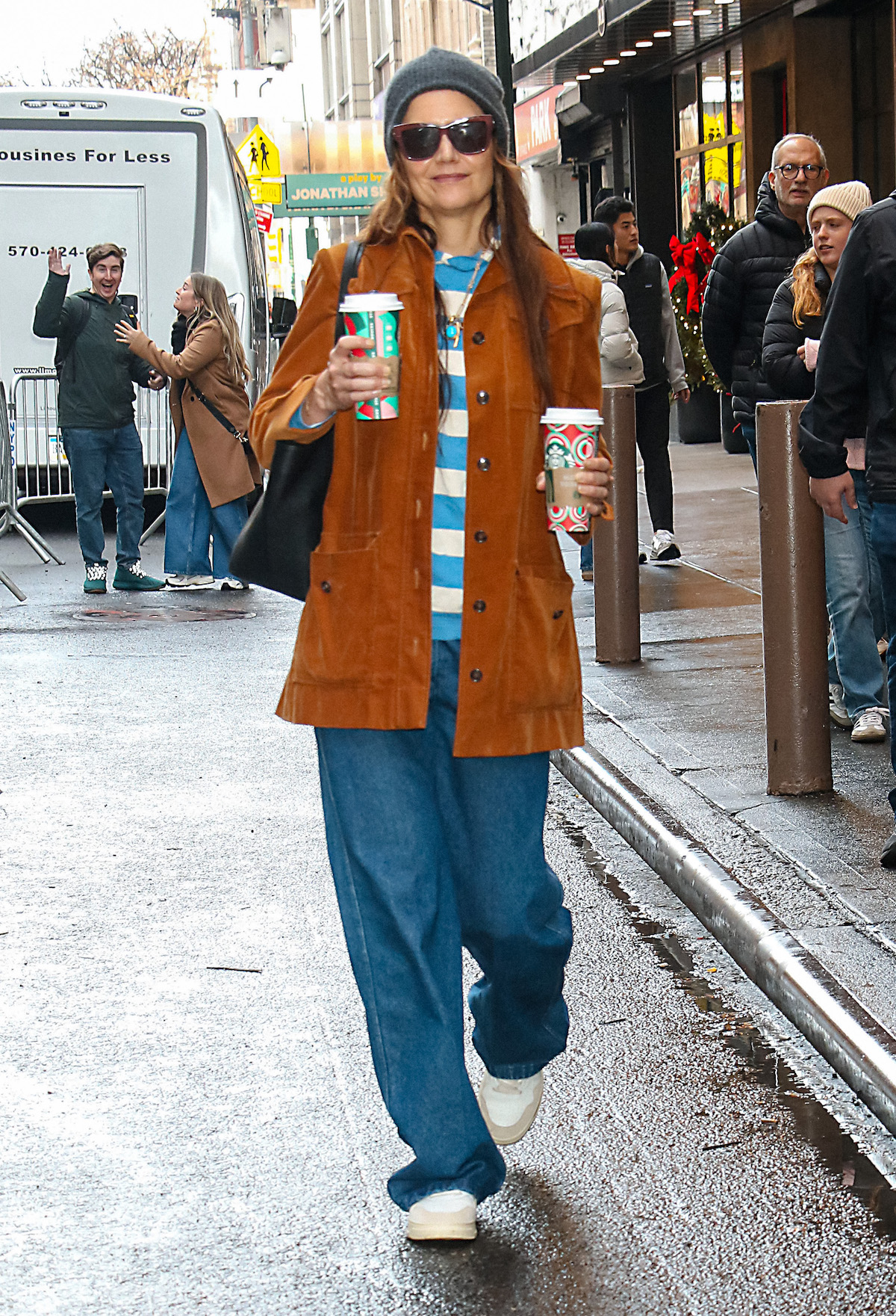 Katie Holmes w damskich jeansach baggy w kolorze królewskiego błękitu, z torebką i kubkami kawy na ulicy.