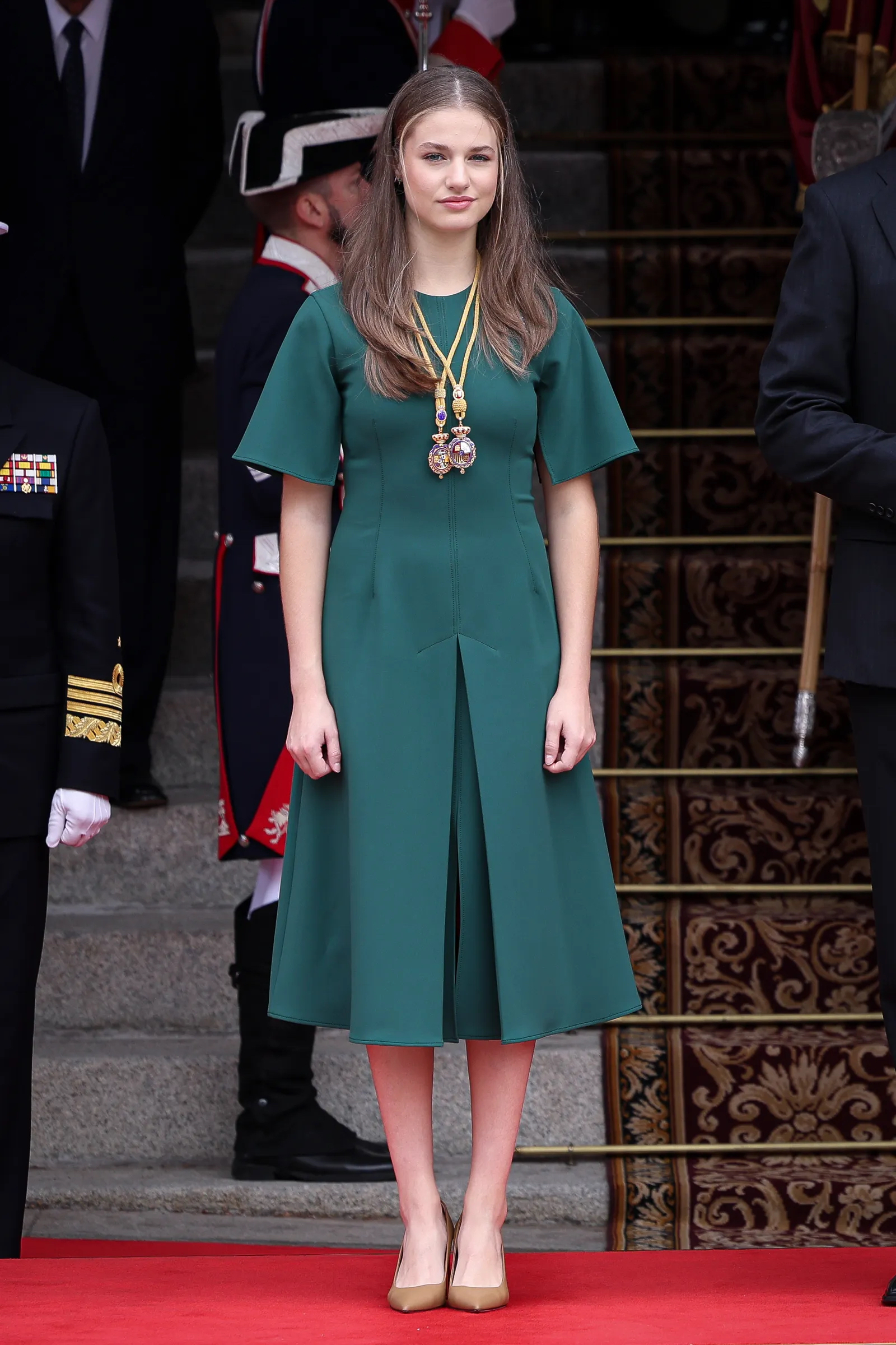 Księżniczka Eleonora z Hiszpanii stoi na czerwonym dywanie, ubrana w zieloną sukienkę, z medalami na szyi.