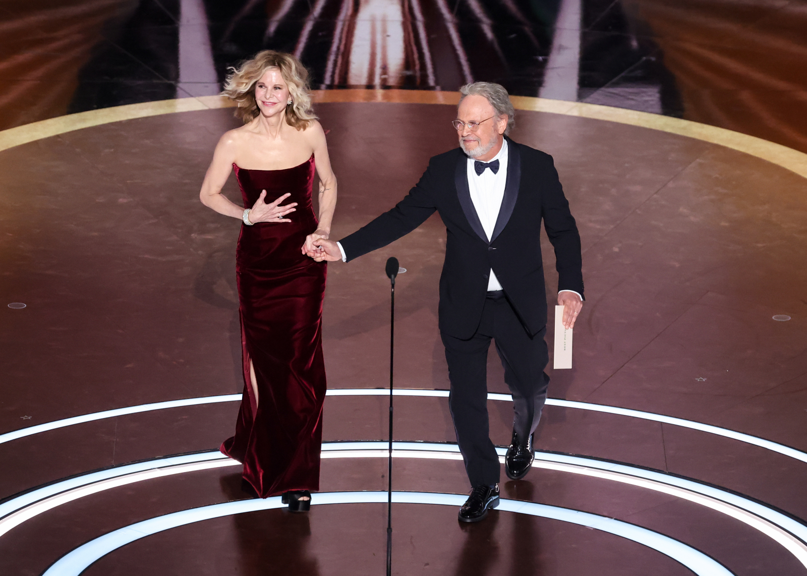 Meg Ryan i Billy Crystal na scenie podczas ceremonii oscarowej. Ryan w długiej, czerwonej sukni, Crystal w smokingowym garniturze.