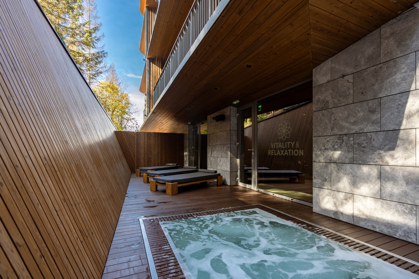 Strefa wellness Hotelu Swissôtel Poiana Brașov z leżakami i jacuzzi na tle drewnianej architektury.