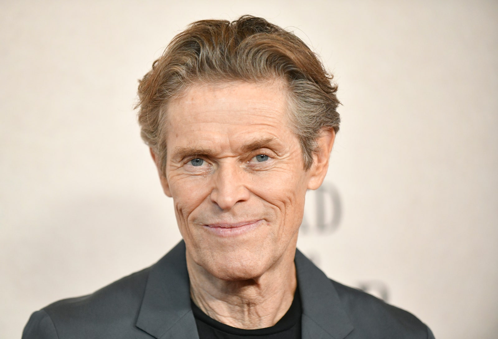 Willem Dafoe w szarej marynarce i czarnym t-shircie