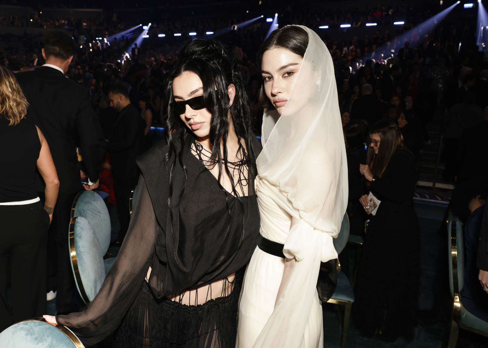 Charli XCX i Gracie Abrams w gotyckich sukienkach, pozujące w tłumie, z efektownym oświetleniem w tle na gali Grammy 2025.