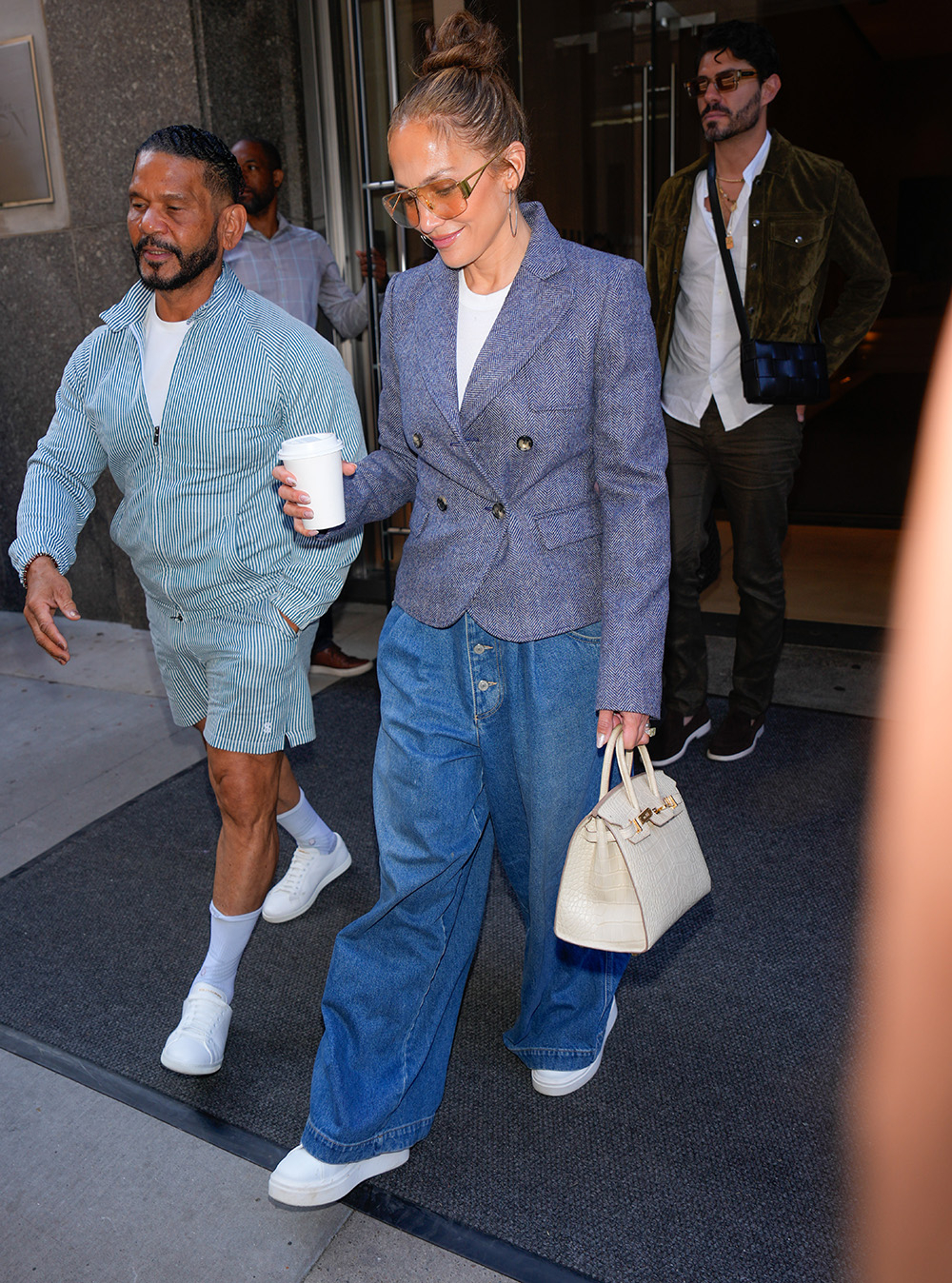 Jennifer Lopez w luźnych, baggy jeansach, trzymając kubek kawy, wychodzi z budynku.