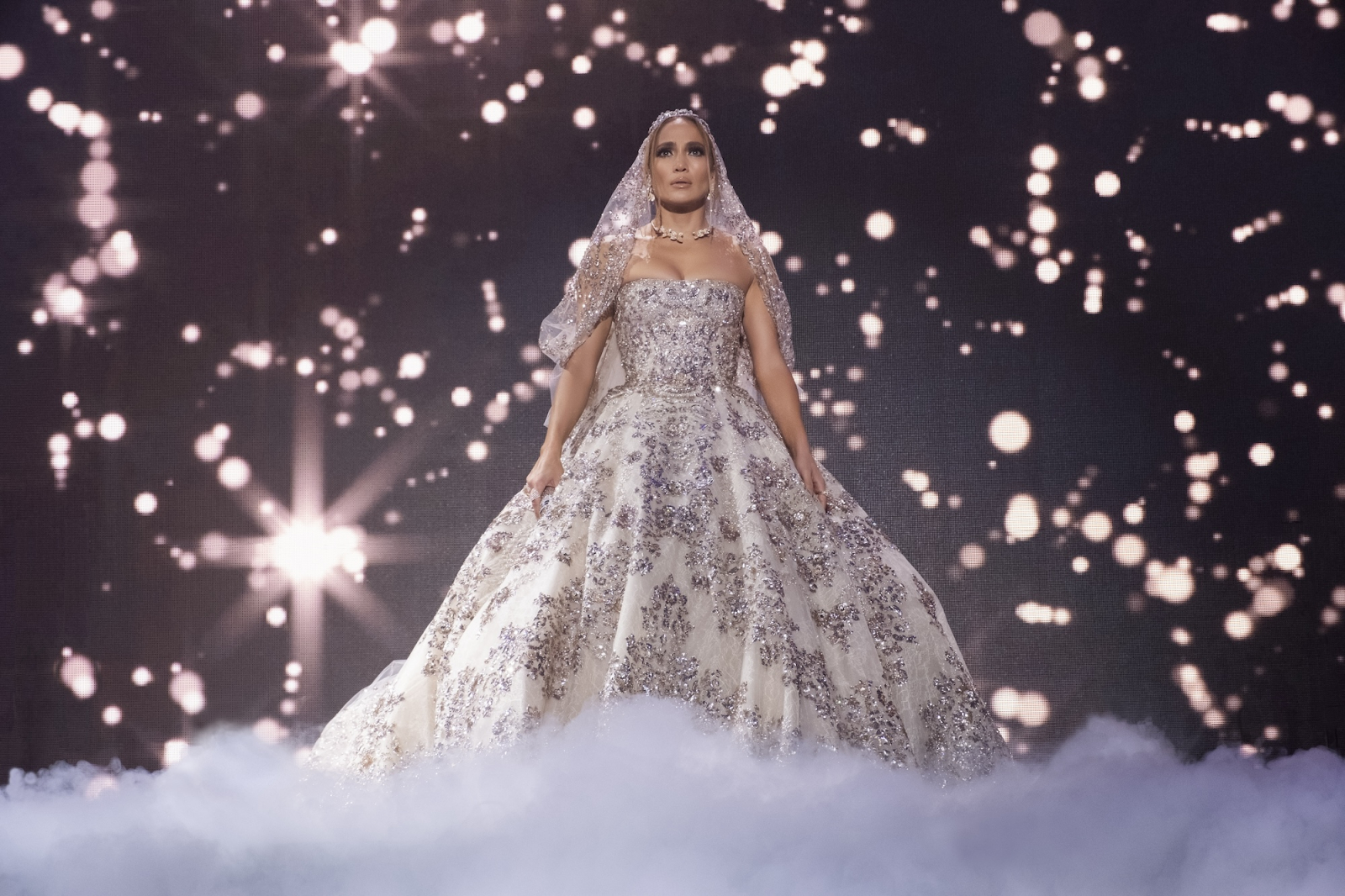 Kadr z filmu „Wyjdź za mnie” z 2022 roku, przedstawiający kobietę w eleganckiej, zdobionej sukni (Jennifer Lopez) na tle świecących punktów.