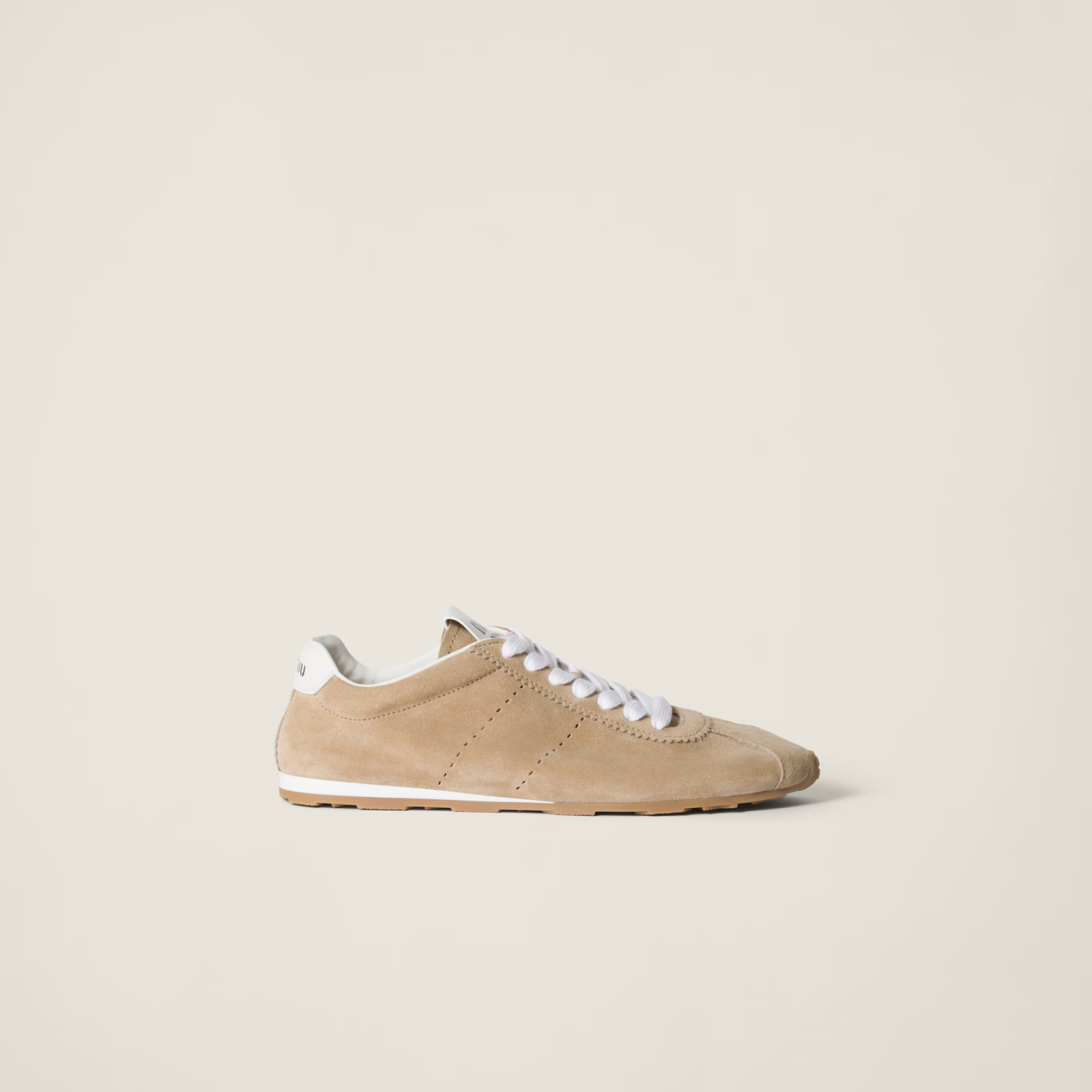 Beżowe sneakersy Miu Miu z białymi sznurówkami, wykonane z zamszu, minimalistyczny design.