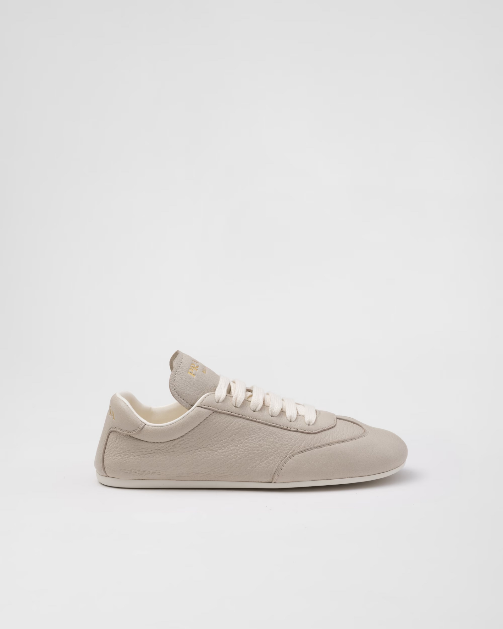 Beżowe sneakersy Prada z białymi sznurówkami, minimalistyczny design, skórzana cholewka.