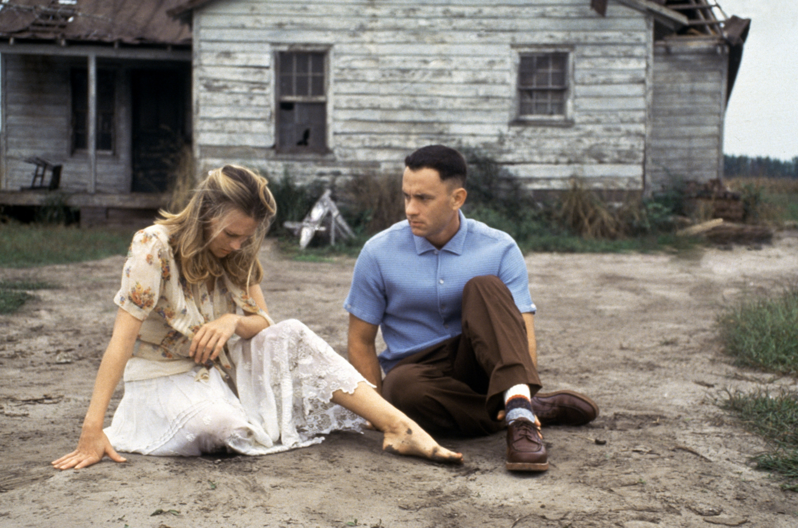 Kadr z filmu „Forrest Gump” w reżyserii Roberta Zemeckisa z 1994 roku: dwoje bohaterów granych przez Robin Wright i Toma Hanksa siedzi na ziemi przed starym domem, wyrażając smutek i zamyślenie.