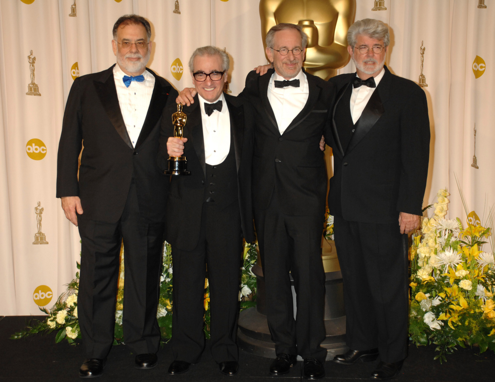 Francis Ford Coppola, Martin Scorsese, Steven Spielberg i George Lucas pozują razem na gali, w tle statuetka Oscara.