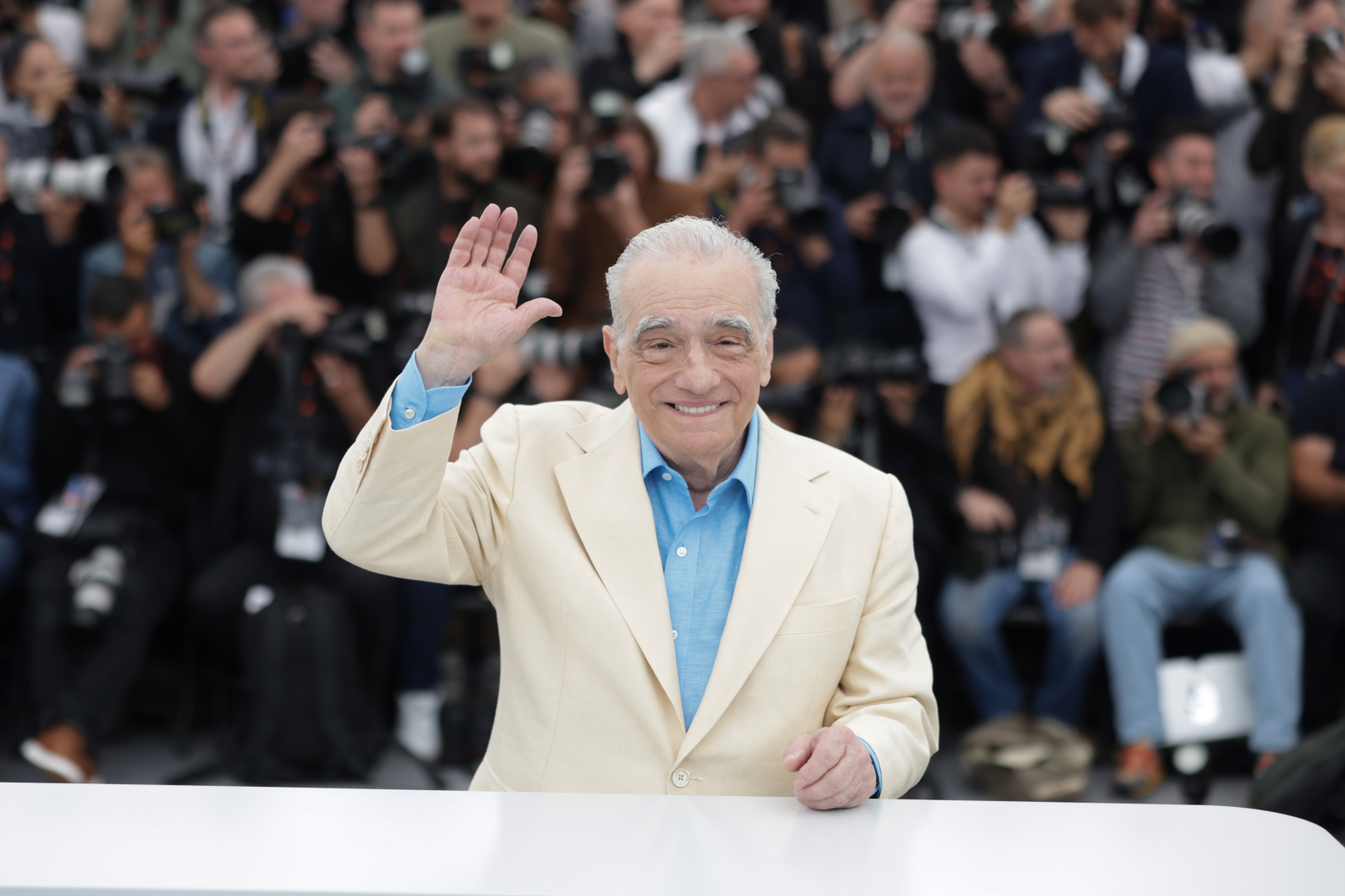 Reżyser Martin Scorsese macha do fanów i paparazzi, w tle widoczni dziennikarze i fotografowie.