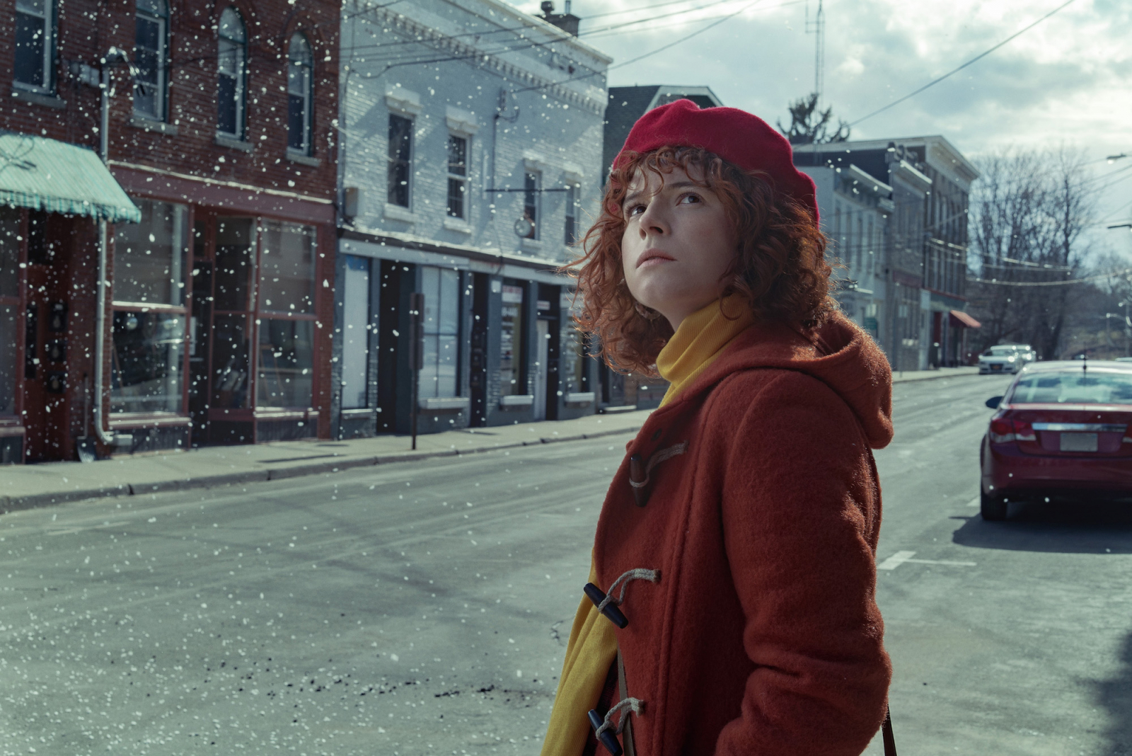 Jessie Buckley w filmie Netflix „Może pora z tym skończyć”, ubrana w czerwoną czapkę i płaszcz, stoi na ulicy w śniegu.