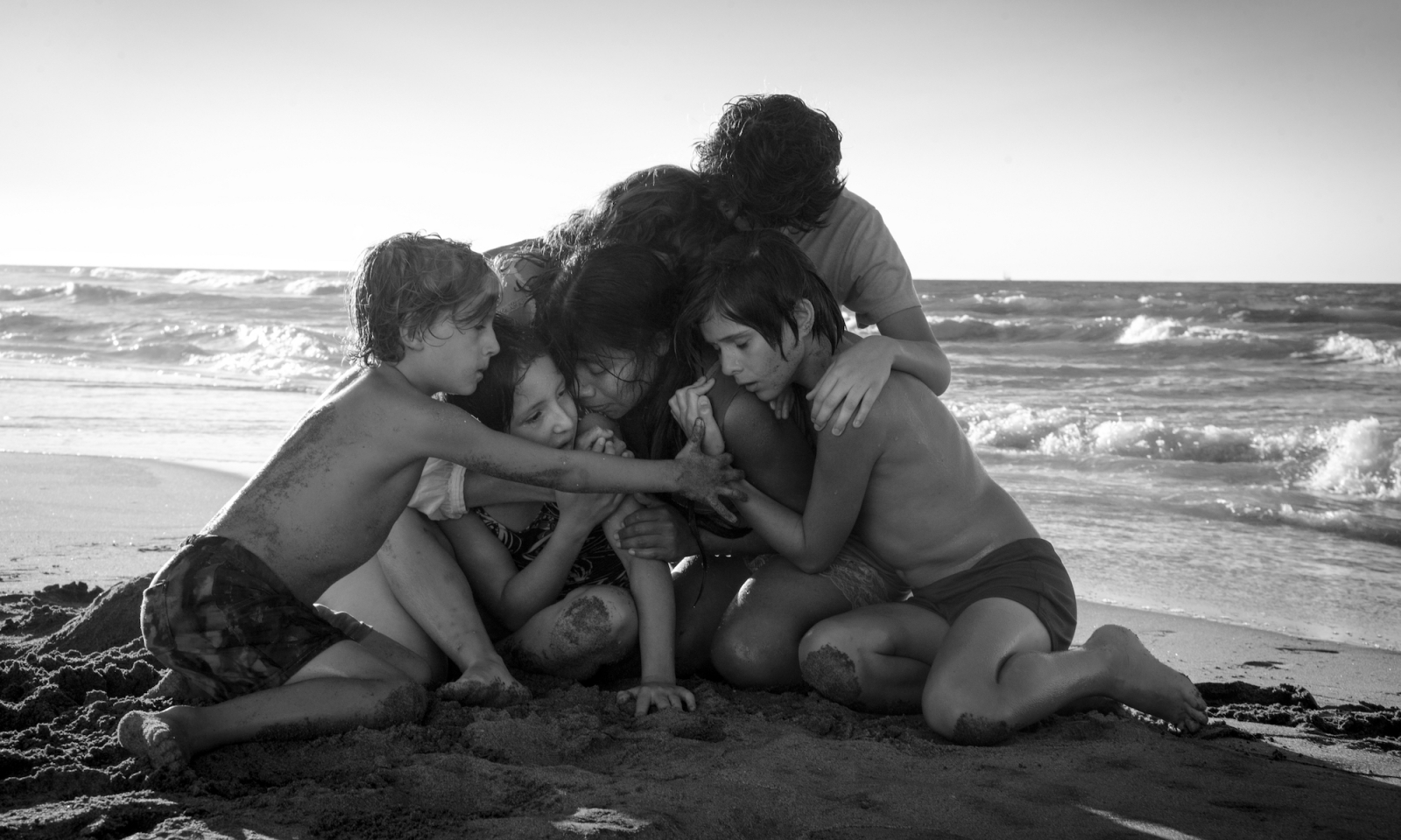 Scena z filmu Netflix „Roma”, w której dzieci przytulają się na plaży, tworząc intymny krąg w otoczeniu morza.