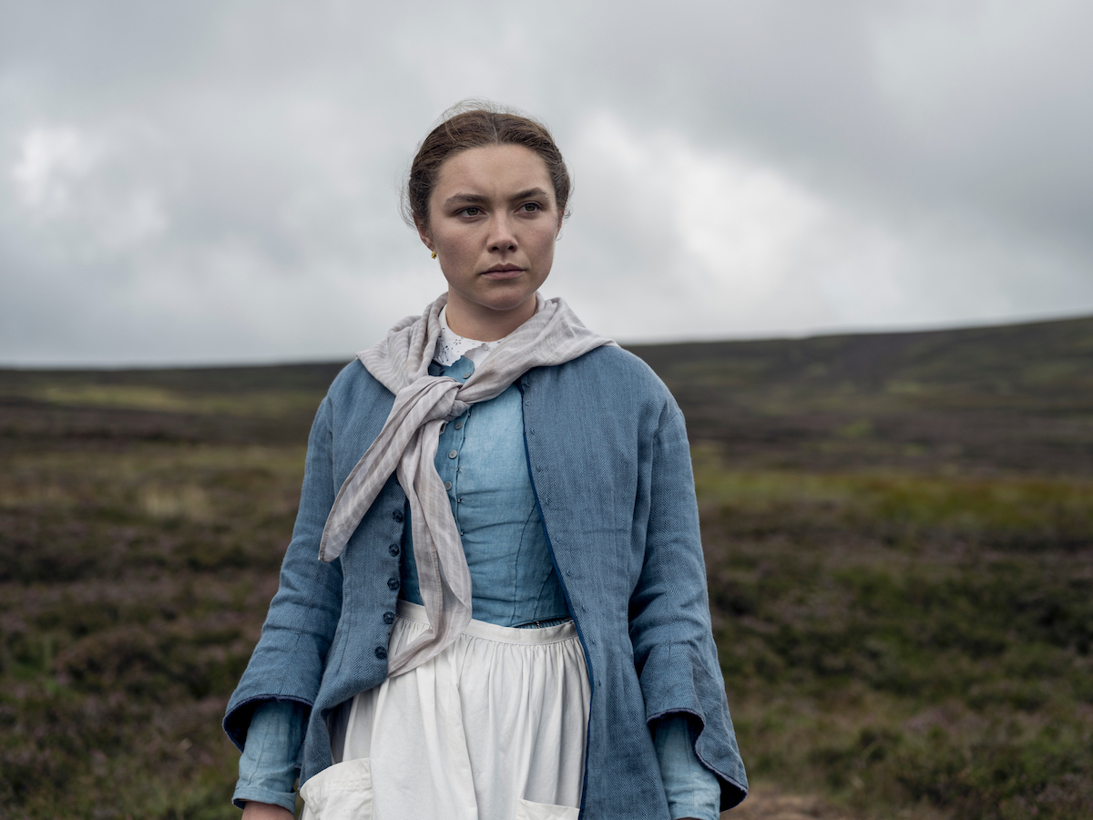 Florence Pugh w roli z filmu Netflix „Osobliwość”, stojąca na tle zielonych pól i pochmurnego nieba.