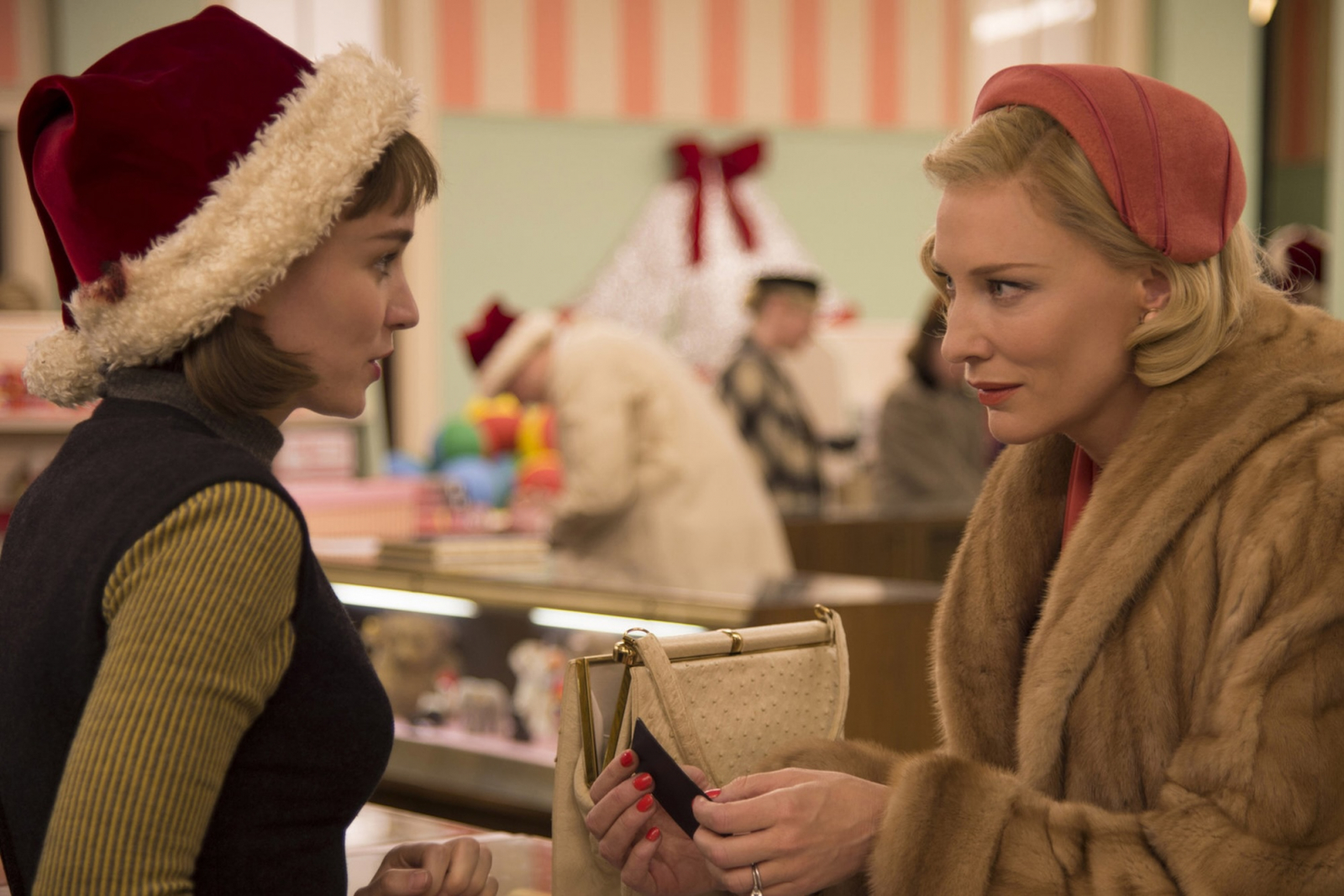 Rooney Mara i Cate Blanchett w świątecznym filmie romantycznym „Carol” rozmawiają w sklepie, otoczone świątecznymi dekoracjami.