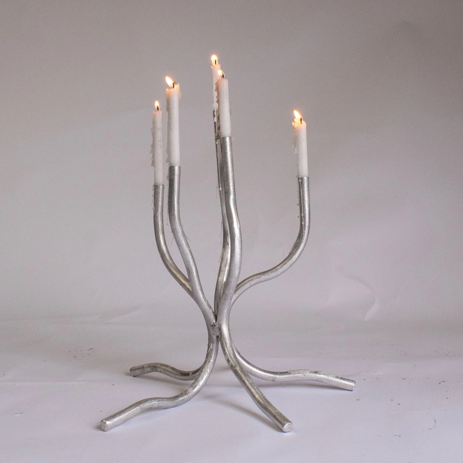 Świecznik Small Candelabra, projektu Josepha Ellwooda, z pięcioma płonącymi świecami w metalowej konstrukcji.