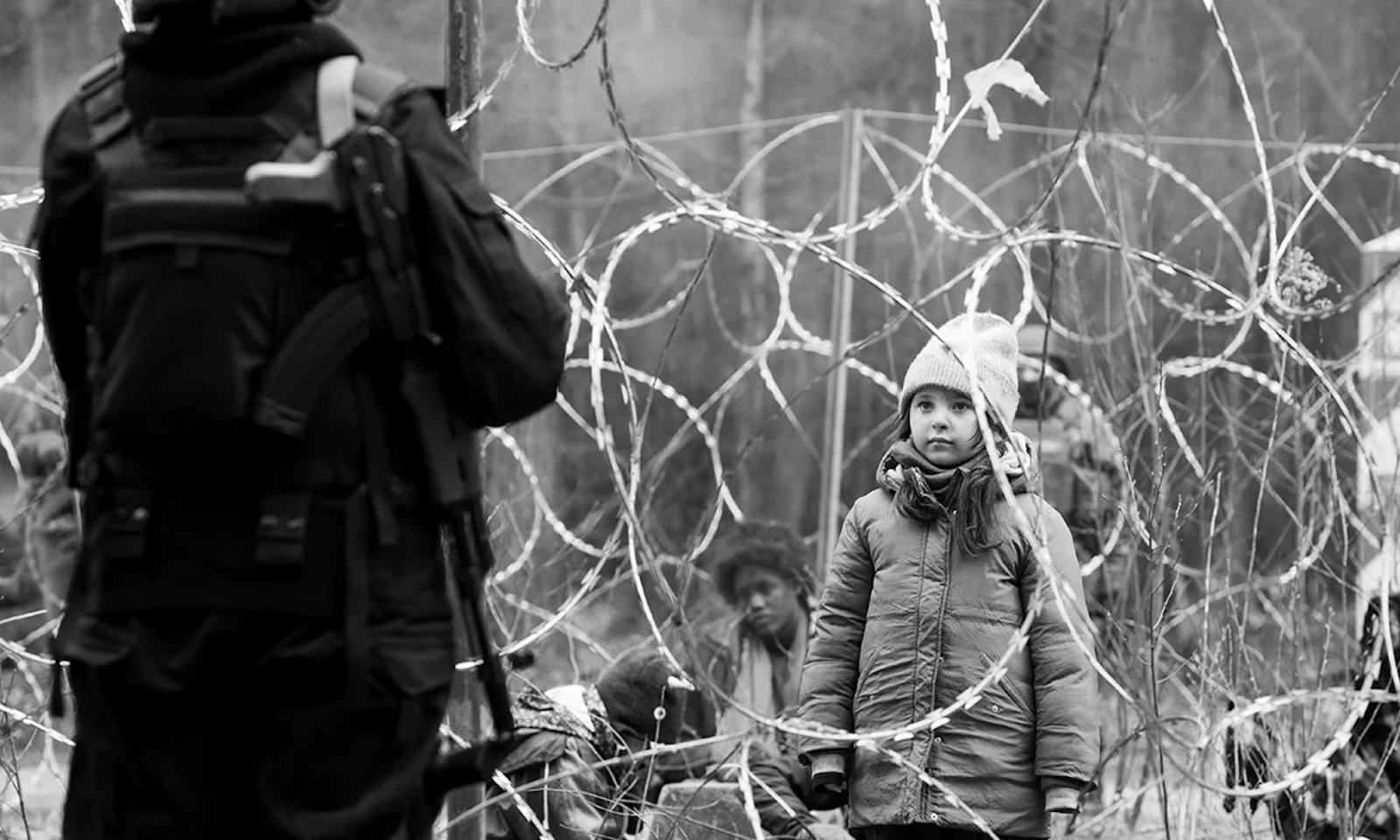 Scena z filmu „Zielona granica” Agnieszki Holland: dziecko w obliczu żołnierza przy ogrodzeniu z drutu kolczastego.