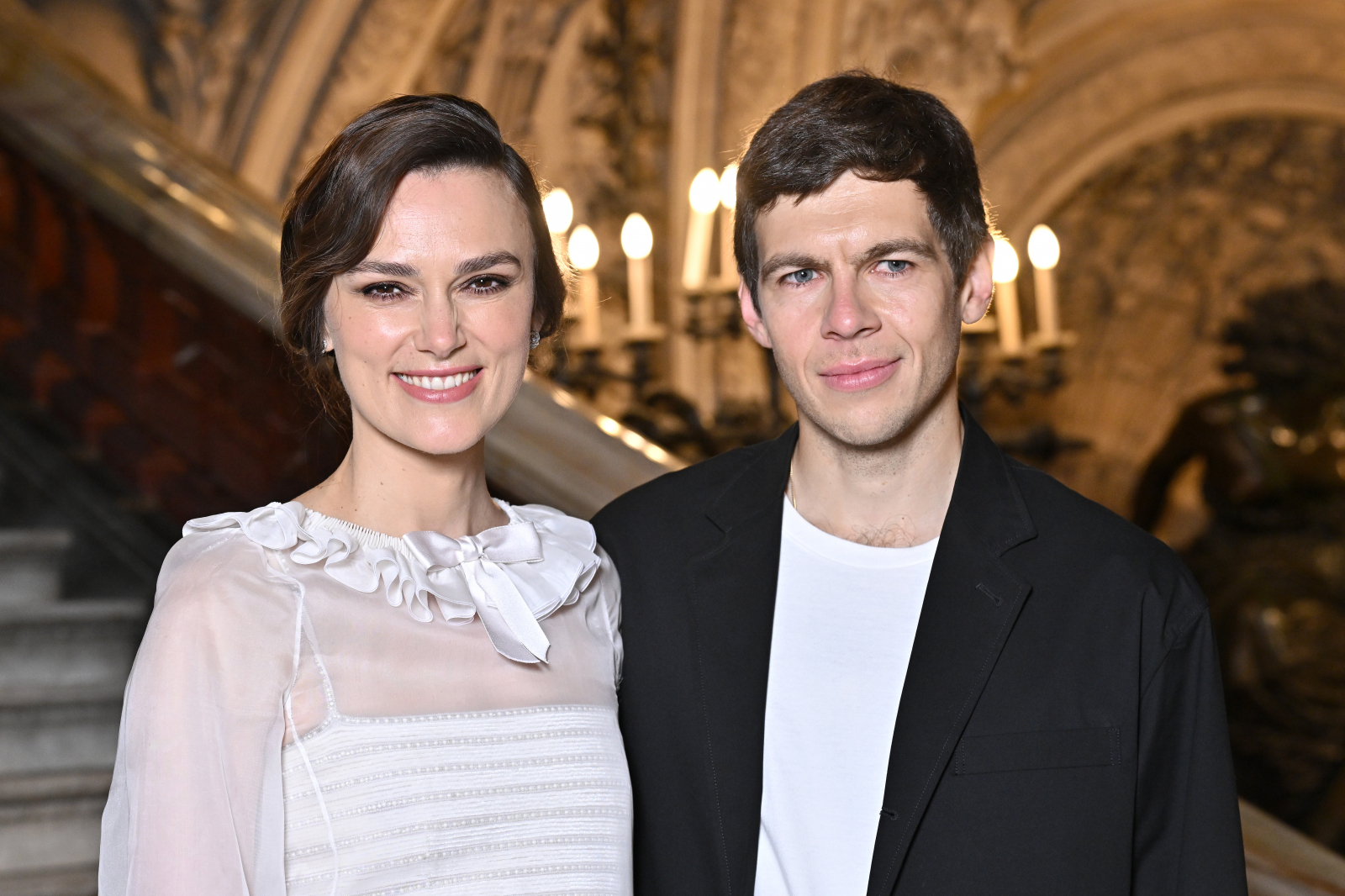 Keira Knightley i James Righton pozują razem w stylowych strojach, w eleganckim otoczeniu z ceglanymi elementami w 2024 roku. 