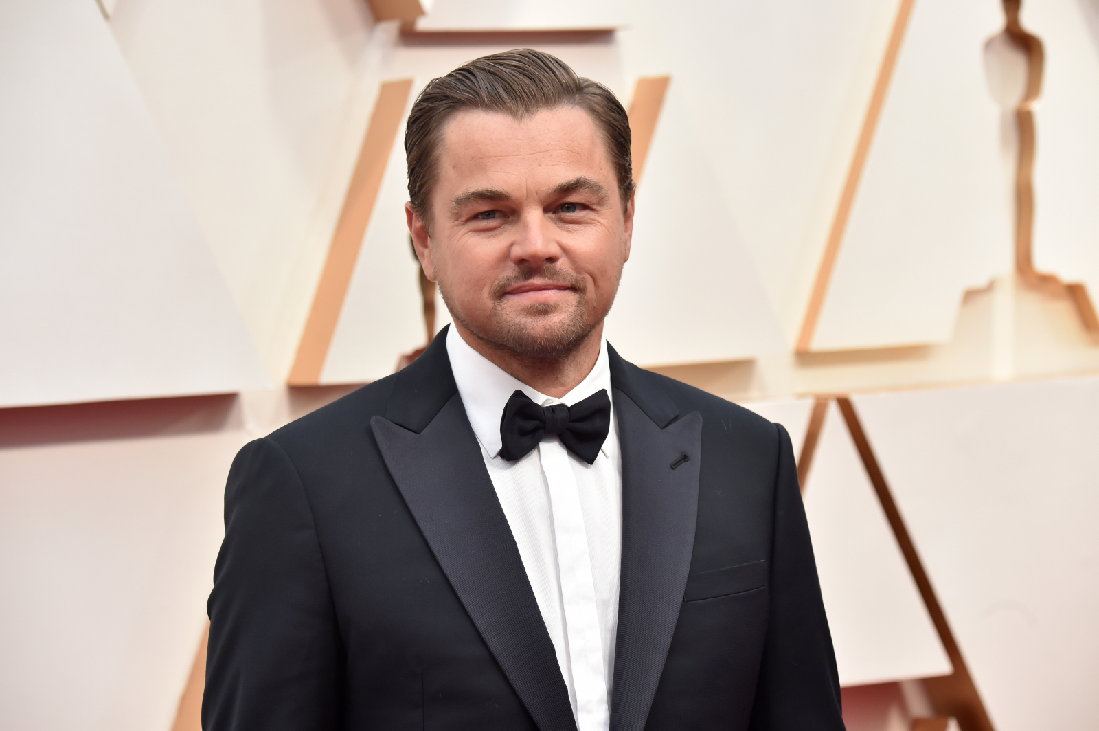 Aktor Leonardo DiCaprio w eleganckim garniturze z muszką na czerwonym dywanie podczas ceremonii wręczenia nagród.