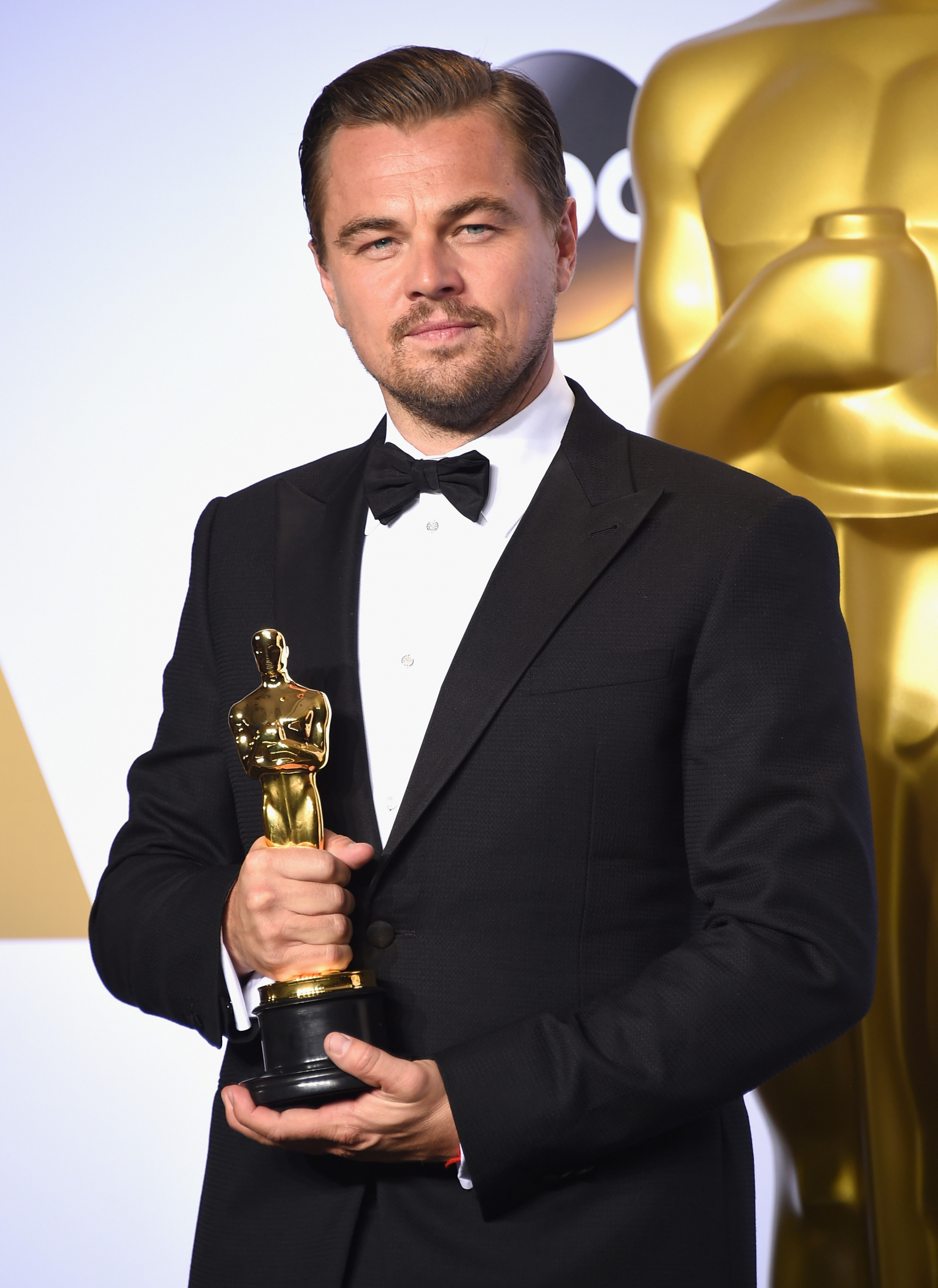 Leonardo DiCaprio z Oscarem za rolę w filmie „Zjawa”, 2016 rok, na tle złotej statuetki.