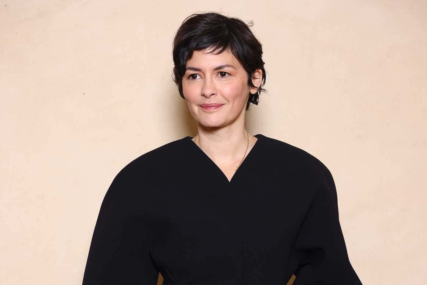 Audrey Tautou pozuje do zdjęcia podczas pokazu kolekcji Jacquemusa, ubrana w czarną, dopasowaną w talii marynarkę, ma na sobie delikatny makijaż i krótkie, ciemne włosy.