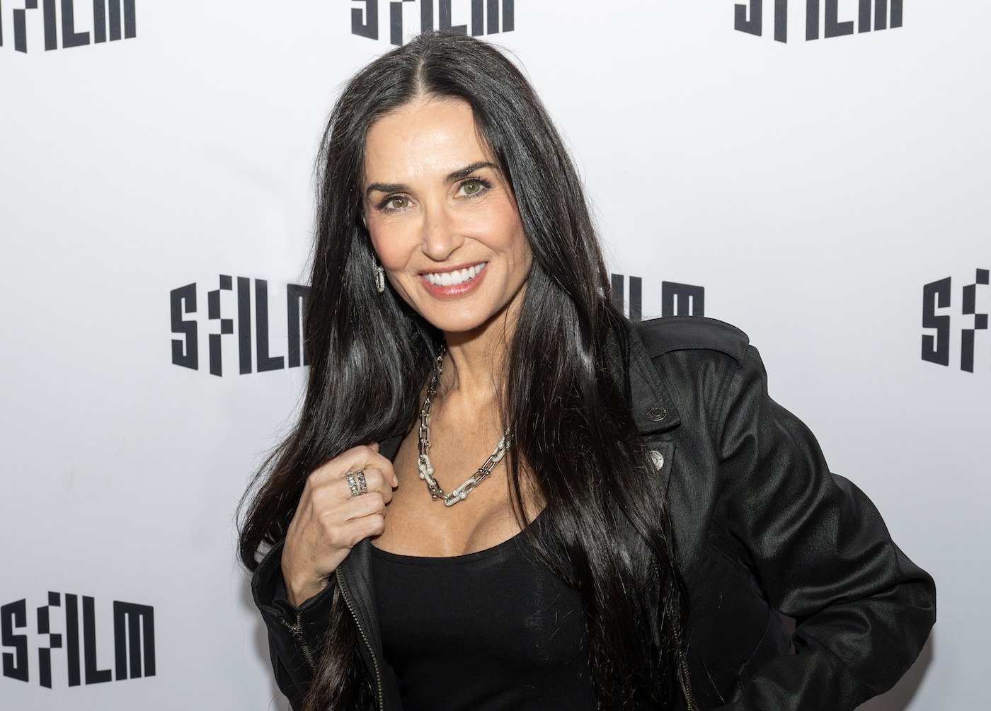 Demi Moore w czarnej sukience Zac Posen dla marki Gap i czarnej kurtce motocyklowej, uśmiecha się pozując.