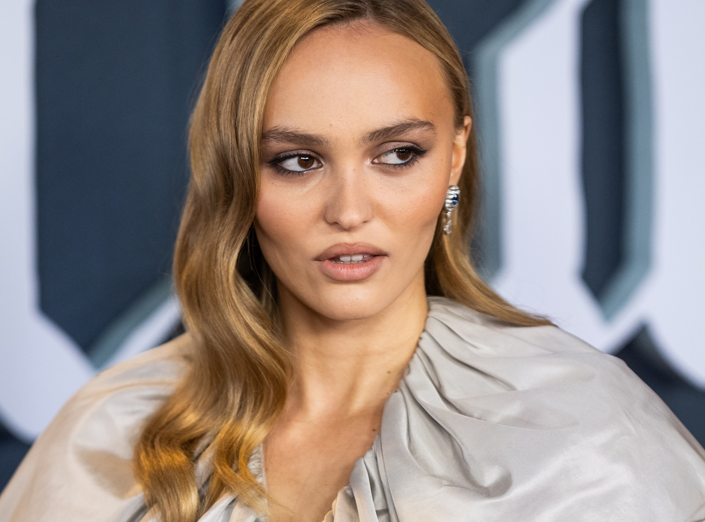 Lily-Rose Depp z gładko zaczesanymi blond włosami, w eleganckiej szarej sukni, pozuje podczas premiery filmu "Nosferatu" w Londynie.