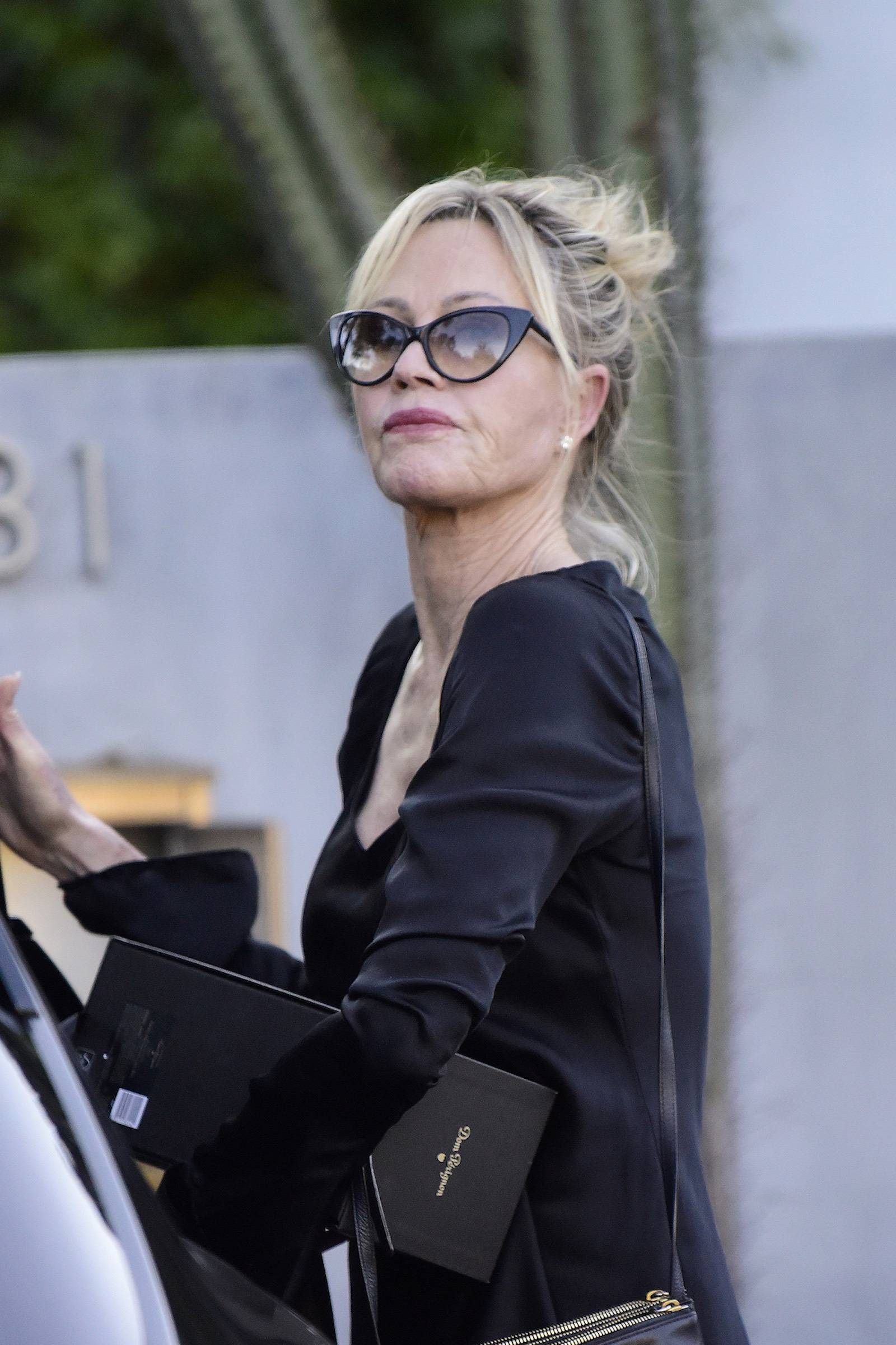 Melanie Griffith w okularach przeciwsłonecznych i czarnej sukience wsiada do samochodu.