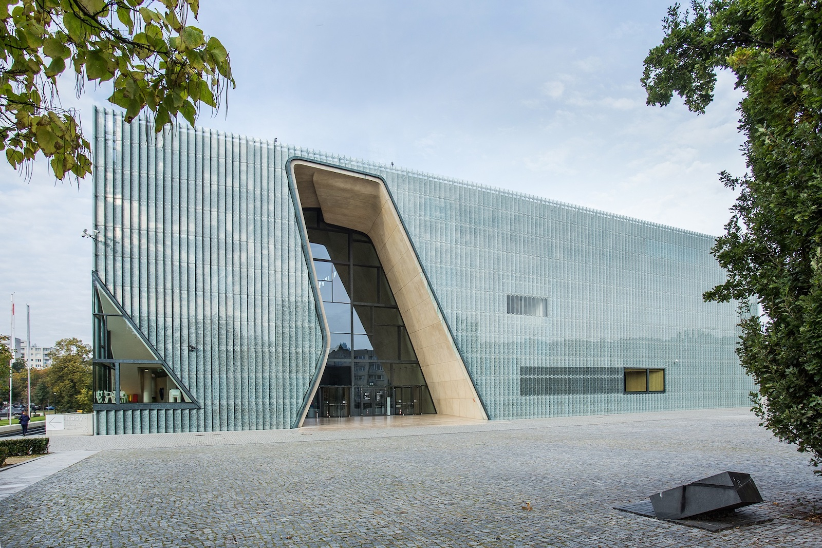 Muzeum Historii Żydów Polskich POLIN, nowoczesny budynek z dużymi przeszkleniami, otoczona zielenią.