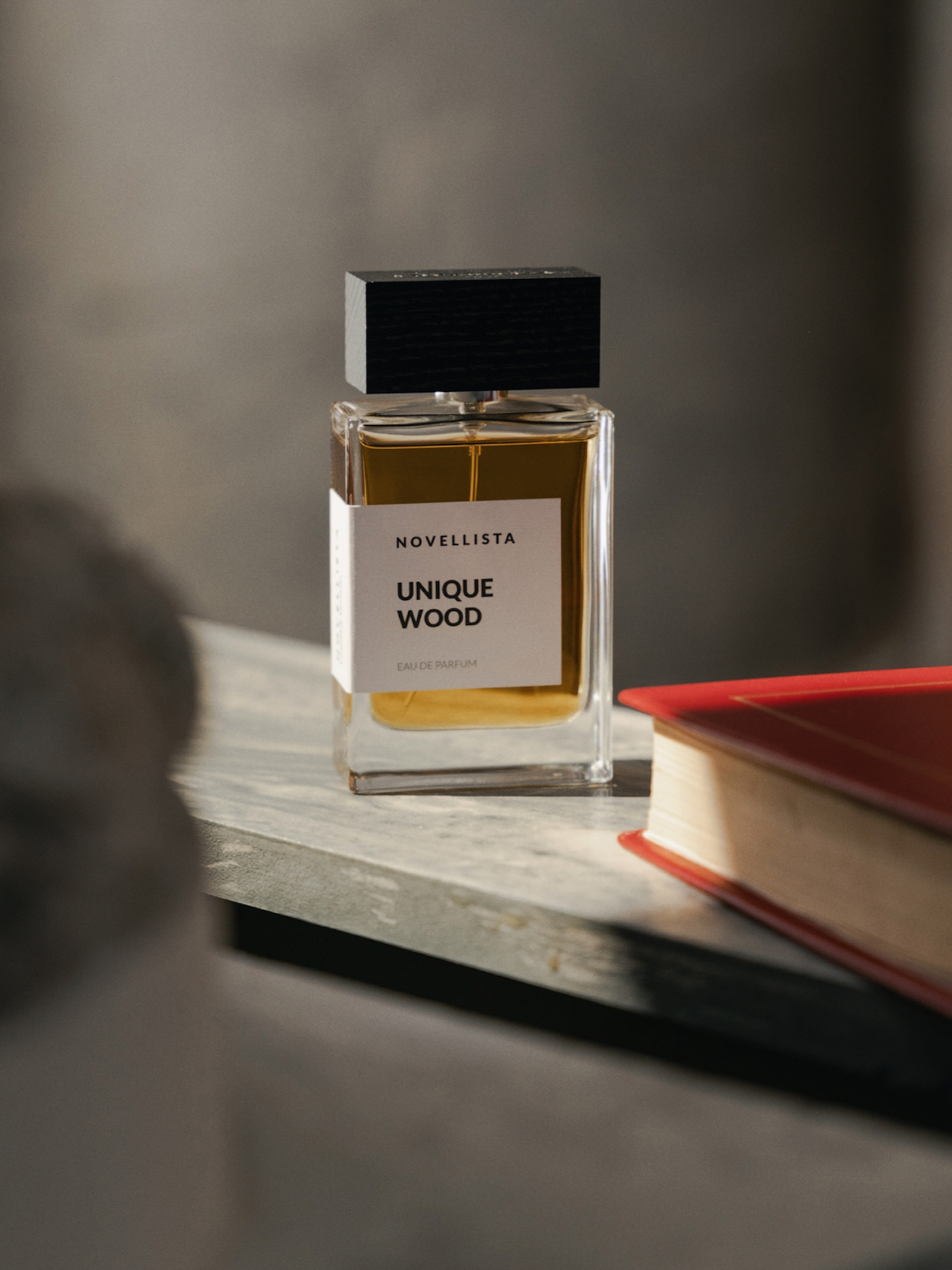 Flakon perfum Novellista Unique Wood na drewnianym stole obok książki w czerwonej okładce.