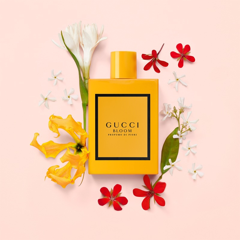 Perfumy Gucci Bloom Profumo di Fiori na różowym tle, w otoczeniu kwiatów.