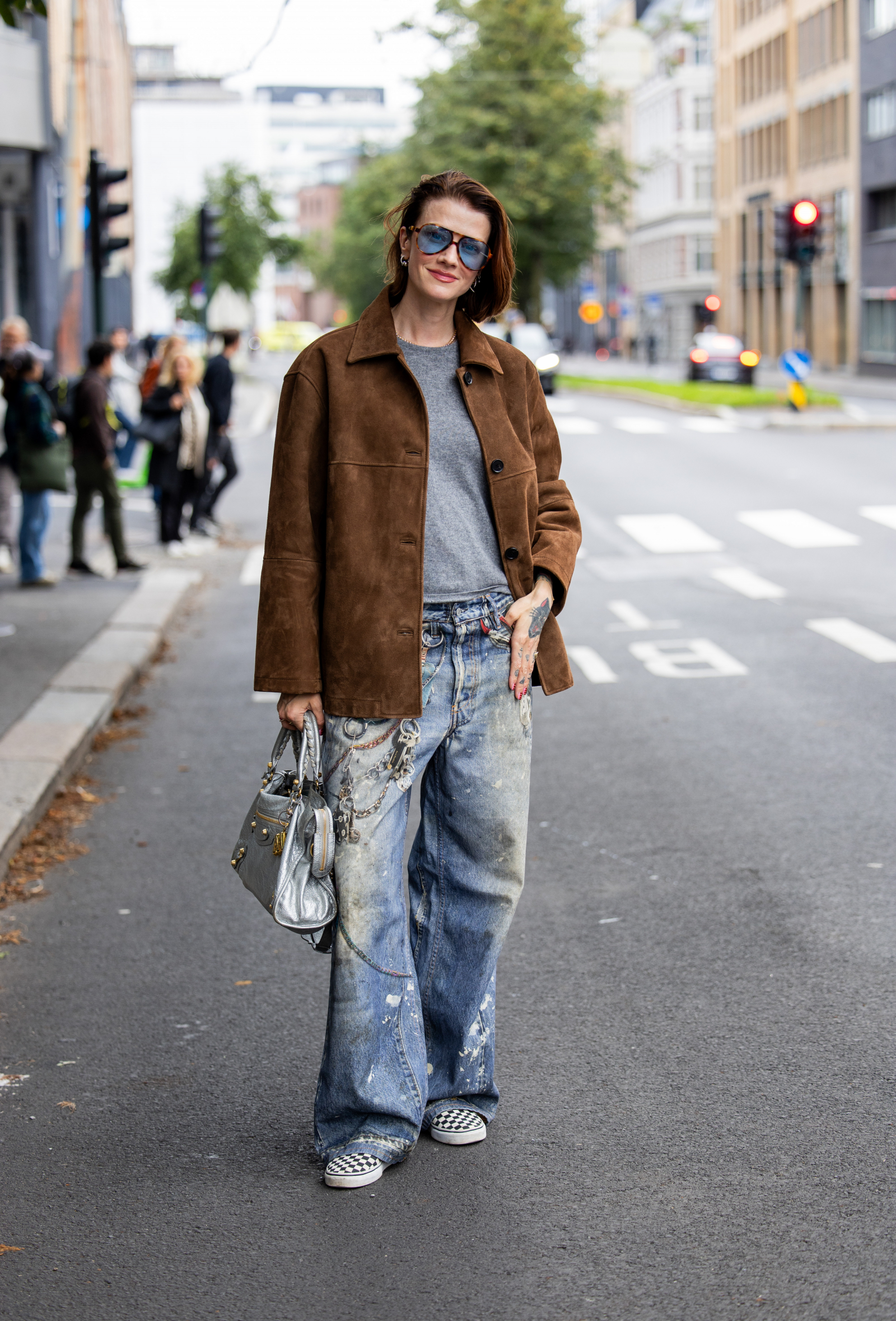 Stylizacja z baggy jeansami i sneakersami, brązową kurtką oraz torebką. Modelka na ulicy, w miejskim otoczeniu.