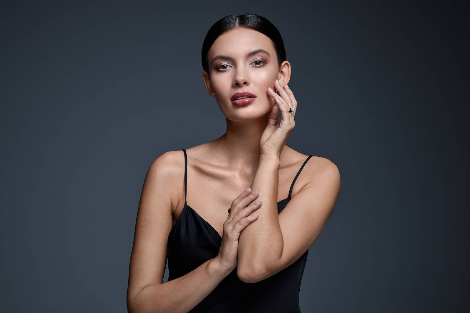 Modelka w czarnej sukience, dotykająca twarzy rękoma.