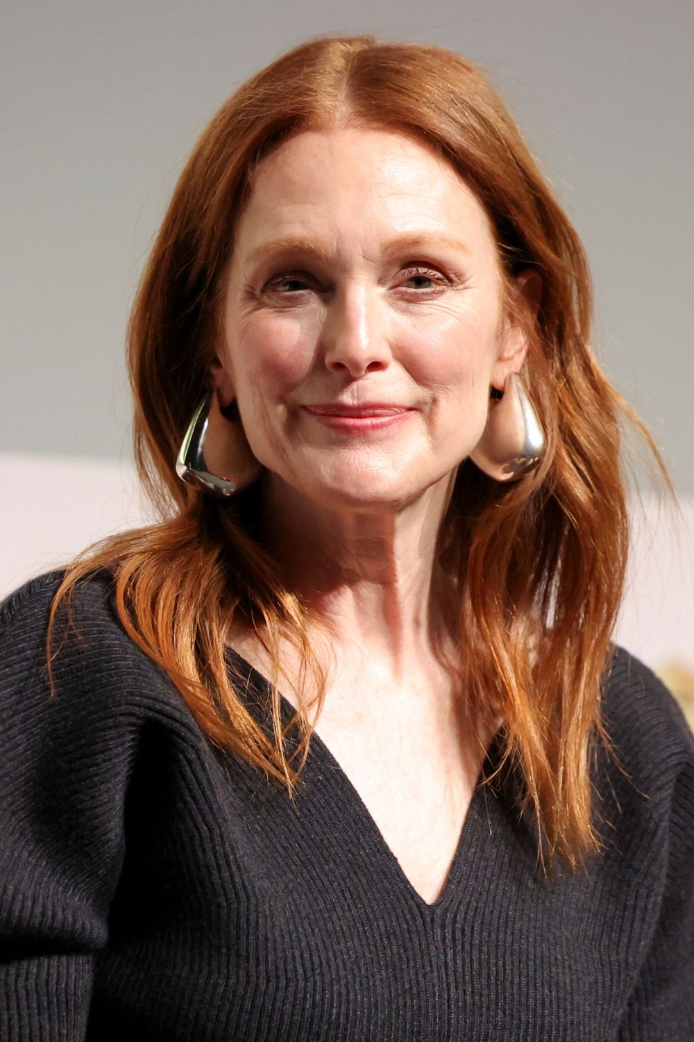 Julianne Moore z uśmiechem, w czarnej bluzce i okazałych kolczykach XXL.