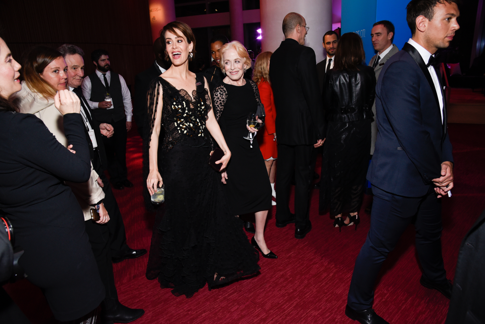 Sarah Paulson w czarnej sukni z koronką, w towarzystwie Holland Taylor, uśmiechają się na eleganckim wydarzeniu.