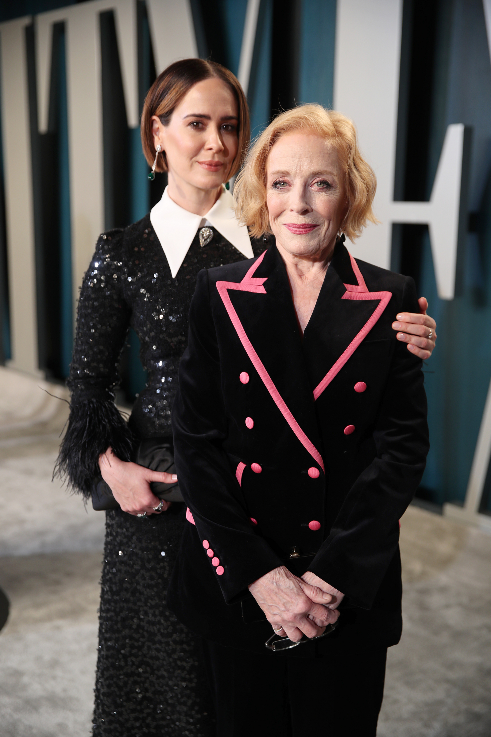 Sarah Paulson i Holland Taylor pozują razem, uśmiechając się do kamery, w eleganckich strojach.