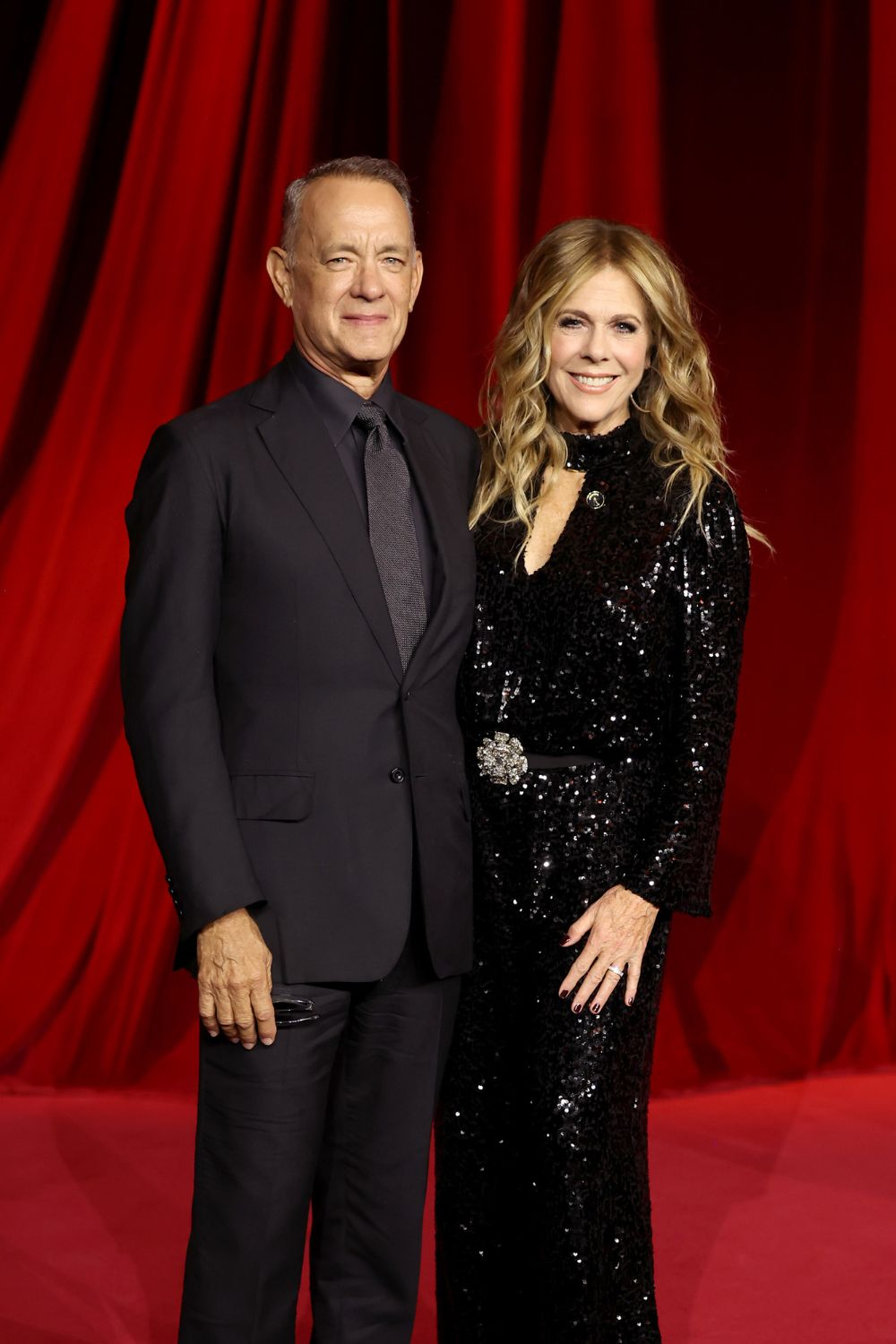 Tom Hanks i Rita Wilson pozują na czerwonym dywanie, ubrani w eleganckie, wieczorowe stroje.