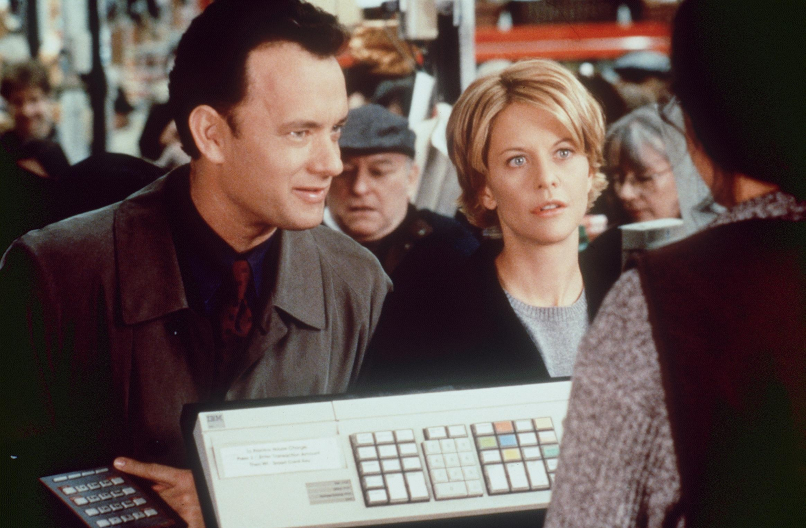 Tom Hanks i Meg Ryan rozmawiają, otoczeni przez innych ludzi.